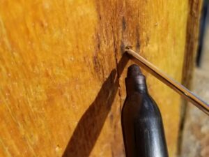 Close-up of a steak skewer inserted into a log, with a sharpie used to mark the skewer at the point where it hits solid wood, demonstrating a method to measure the depth of log rot in a log cabin.