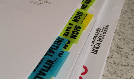 A stack of documents with colorful tabs labeled "SIGN," "INITIAL," and "KEEP FOR YOUR RECORDS."