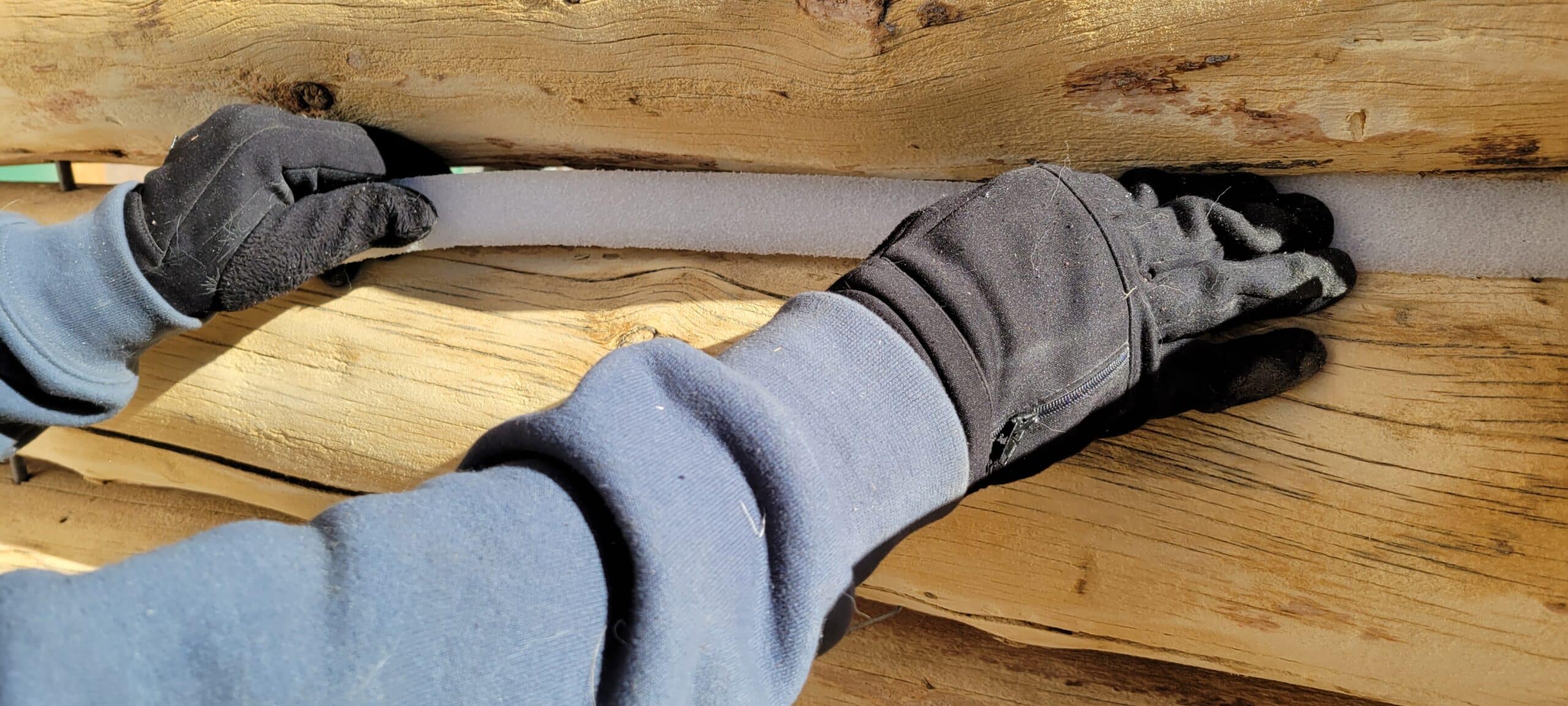 This is an image of a Log Master installing grip strip between a log gap on a log cabin restoration before the logs are stained after media blasting.