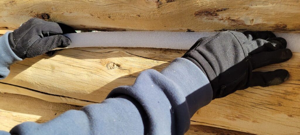 This is an image of a Log Master installing grip strip between a log gap on a log cabin restoration before the logs are stained after media blasting.