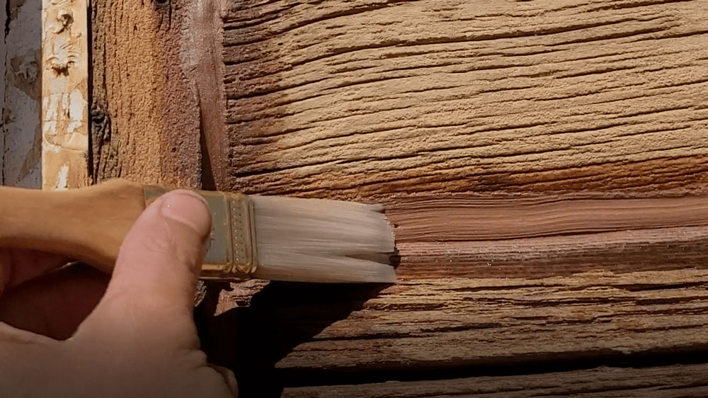 In this image, a Log Master is using a damp brush to smooth out the caulking after applying so it blends in seamlessly with the cabin logs.